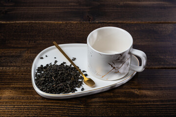 loose tea in a saucer next to a mug on a wooden background with different lighting