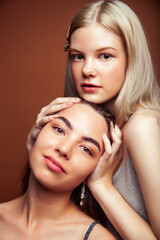 two pretty diverse girls happy posing together: blond and brunette on brown background, lifestyle people concept