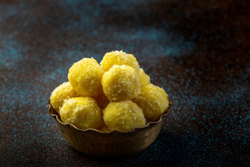 saffron flavoured desiccated coconut ladoo in a traditional metal bowl