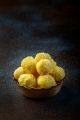 saffron flavoured desiccated coconut ladoo in a traditional metal bowl