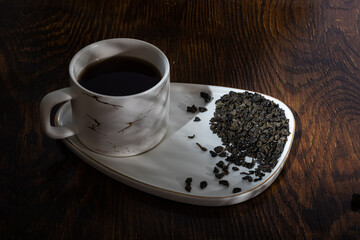 loose tea in a saucer next to a mug on a wooden background with different lighting