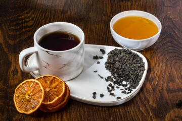 loose tea into the saucer next to the cup and sweets on the wooden background with different lighting