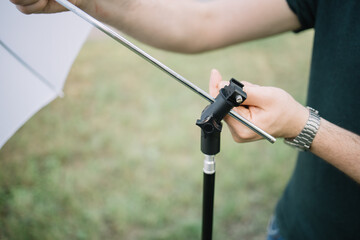 Close-up view of male hands placing umbrella diffuser to stand. Cropped man setting umbrella...