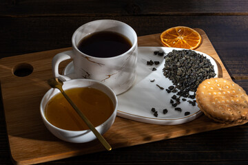 loose tea into the saucer next to the cup and sweets on the wooden background with different lighting