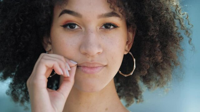 Close-up portrait of pretty African American girl with afro hairstyle zipping lips, locking mouth. Young ethnic model smiles slyly, imitates throwing away key, promises to keep secret, mystery silence