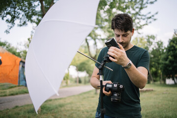 Male photographer setting flash light while holding camera. Man looking at camera and setting flash light on stand while standing in park.