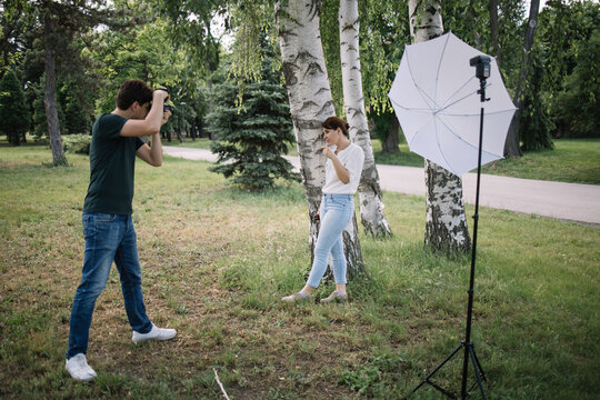 Photographer taking pictures of female model in nature. Man photographer photographing the female model who is leaning against birch tree in forest.