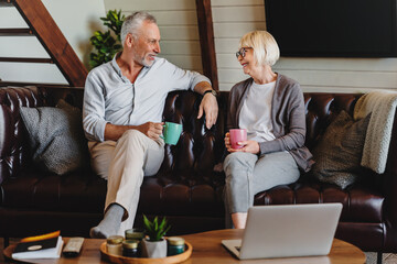 Joyful mature man and woman drinking coffee while resting on couch at home