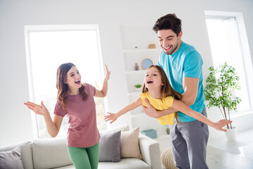 Photo of positive cheerful three people play game dad carry small kid girl she hold hands fly like bird mom show support teach how in house indoors