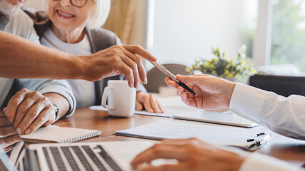 Close up of senior couple singing at home contract. Advisor giving pen to elder man to sign documents
