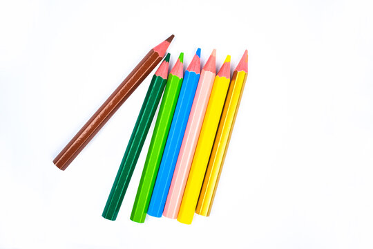 Seven different colored wood pencil crayons scattered on a white background