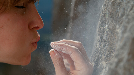 CLOSE UP: Young woman blows excess chalk off her fingertips while climbing.