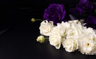 Funeral flowers of white and purple eustoma on a black background. Copy space