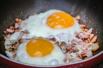 Low angle view view of two eggs sunny side up with bacon in a frying pan as part of breakfast