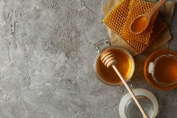 Composition with honeycombs, honey and jars on gray background