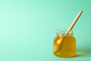 Glass jar of honey with dipper on mint background, space for text