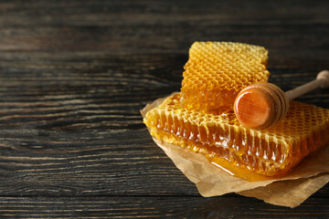 Baking paper with honeycomb pieces and dipper on wooden background