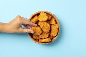 Female hand holds nugget over the blue background with bowl of nuggets