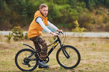 Fototapeta na wymiar Young boy in orange colored jacket sitting on his bike outdoors at daytime