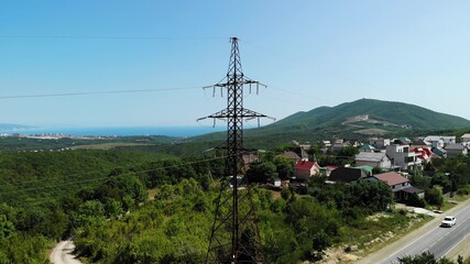 Obraz premium Aerial shot of an electric tower in the countryside among green mountains. The blue sky over the village is connected to electrical wires through a special device. Slow boom down.