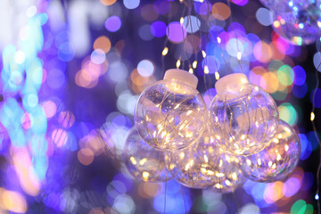 Light bulbs decorated with shiny threads hang against the background of multicolored glitter