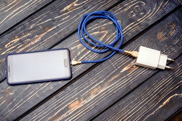 Mobile phone and charger on brown wooden background
