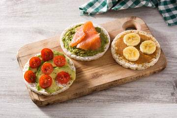 Assortment of ingredients on puffed rice cakes on white wooden table