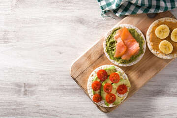 Assortment of ingredients on puffed rice cakes on white wooden table.Top view.Copy space