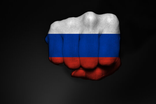 Low key picture of a fist painted in colors of Russian flag on a black background