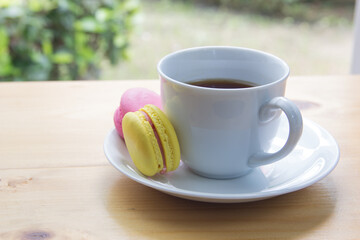 Tea time in the garden. Macaron and coffee in white mug on the table.