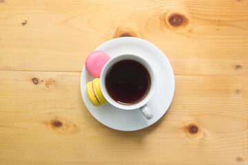 Top view of macaron and tea in white mug on wooden background.