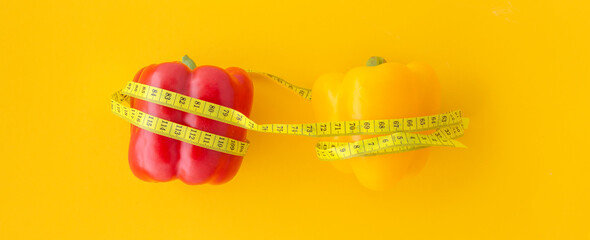 red and yellow peppers with measuring tape on yellow background. Weight loss, slim body, lifestyle concept.