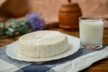 A glass of goat milk and a head of goat milk cheese stand on a wooden table. Cheese at home.