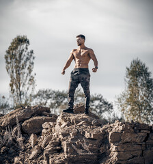 Athlete with perfect torso standing on top of rock. Blue sky above. Sunny day.