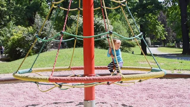 Cute little boy having fun playing on the carousel in the park, beautiful summer sunny day in children playground