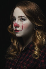 girl in clown make-up on a black background. Portrait of a girl with red hair.