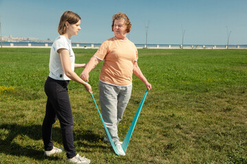 Naklejka na ściany i meble Young woman trainer helps senior woman doing stretching exercises.