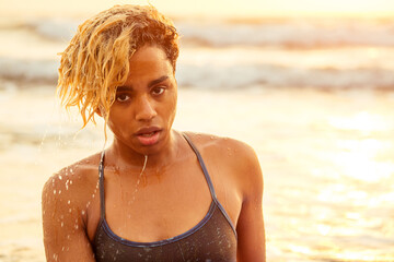 beautiful portrait of african american surfer woman with wet afro blonde curly hair in bikini at sunset on beach