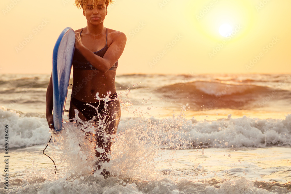 Wall mural afro american woman run with surfboard on beach in goa