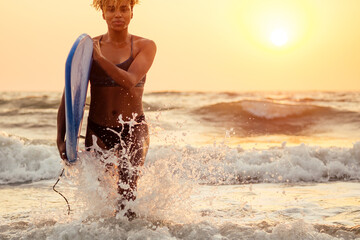 afro american woman run with surfboard on beach in Goa