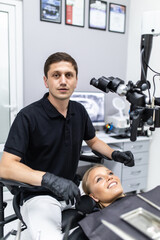 Handsome dentist sitting in chair, posing, looking at camera. Dentist man working in private dentistry clinic with modern equipment, professional microscope.