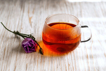 black tea in a transparent Cup next to a purple flower on a light wooden background