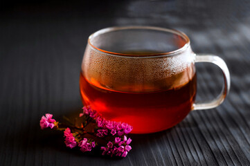black tea in a transparent Cup next to a purple flower on a dark wooden background