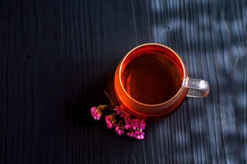 black tea in a transparent Cup next to a purple flower on a dark wooden background