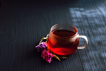black tea in a transparent Cup next to a purple flower on a dark wooden background