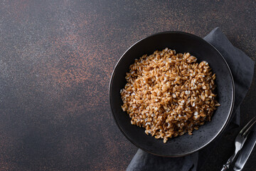 Wholegrain spelt farro in bowl on brown background. Top view.