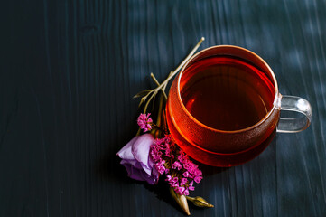 black tea in a transparent Cup next to a purple flower on a dark wooden background