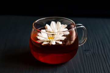 black tea in a transparent Cup with chamomile on a dark wooden background