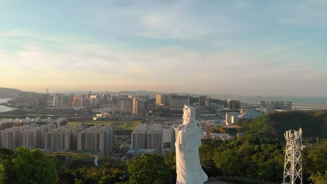 Rotating aerial view of Goddess A-Ma looking over Macau cityscape during sunset