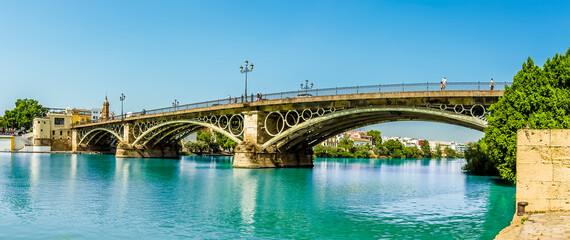 Obraz premium A view on the east bank of the river Guadalquivir towards the Triana Bridge in Seville, Spain in the summertime